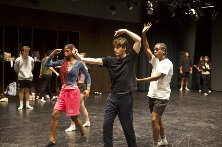 Three Tisch Summer High School Drama students pose in mid-rehearsal with arms curved and raised above their heads